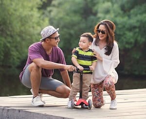 Young family couple with small child on a dock by the water holding child on a scooter.