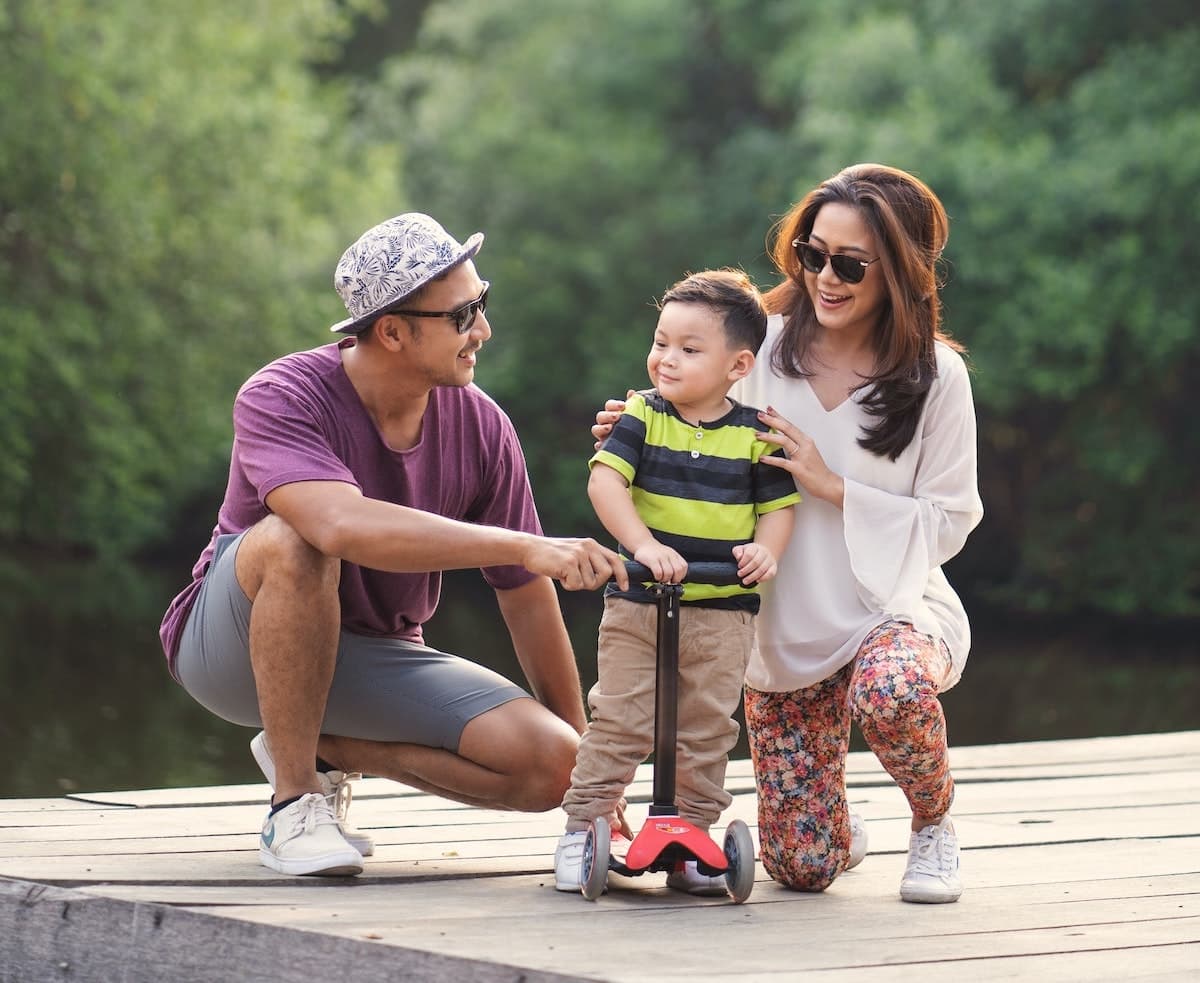 Young family couple with small child on a dock by the water holding child on a scooter. 