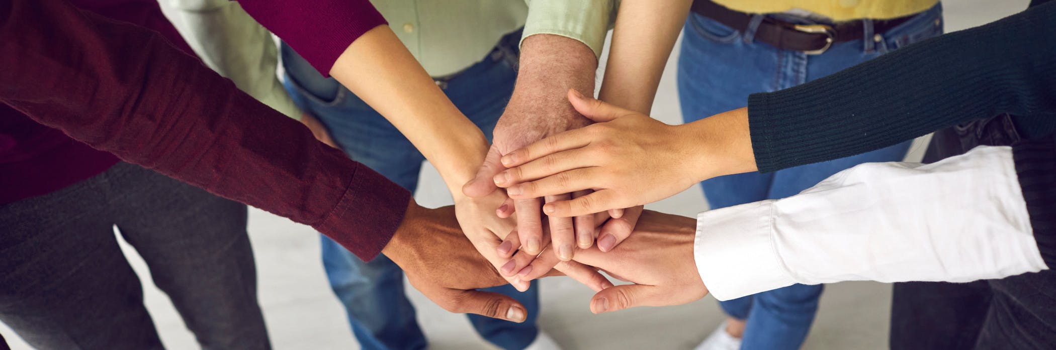 Diverse group of people with their hands together in the center of a circle to show a sense of community and shared work